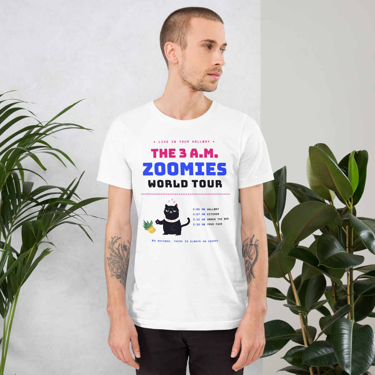 Man wearing a white unisex t-shirt with a black cat knocking over a plant and the words “The 3 A.M. Zoomies World Tour” with a list of tour stops