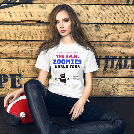 Woman wearing a white unisex t-shirt with a black cat knocking over a plant and the words “The 3 A.M. Zoomies World Tour” with a list of tour stops